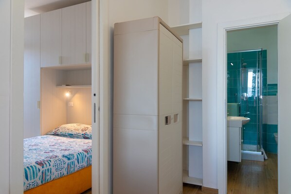 A compact bedroom with a bed, a wardrobe, and a bathroom with a shower and sink.