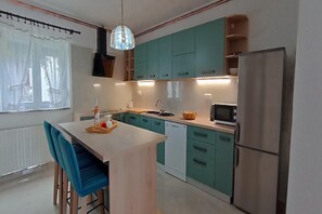 A kitchen with teal cabinets, a white countertop, a sink, a microwave, and a refrigerator.