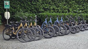 Una fila de bicicletas estacionadas frente a un letrero verde con un símbolo de rayo, que indica una estación de carga.