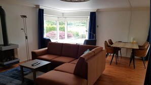 Una sala de estar con sofá, mesa de centro, chimenea, mesa de comedor con sillas y vista a través de un ventanal.