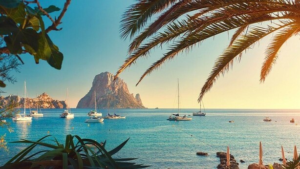 A coastal scene with boats, a rocky shoreline, and a prominent mountain in the background.