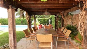 An outdoor patio with a wooden table and wicker chairs, surrounded by stone pillars and a stone wall.