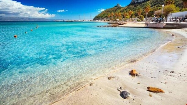 A beach with clear turquoise water, a sandy shore, and a rocky hill in the background. - Civico36 Feels Like Home (Cagliari)