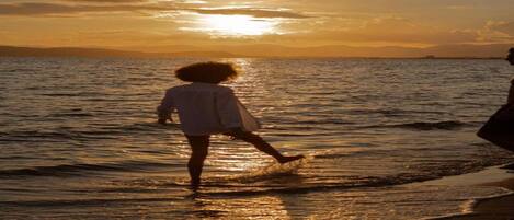 A sunset over a calm sea with a person walking in the water.