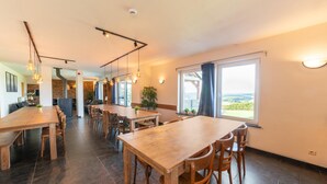 Un vaste espace dédié à la salle à manger, avec de nombreuses tables et chaises en bois, de grandes fenêtres dotées de rideaux et des luminaires suspendus.