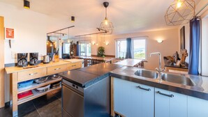 Une cuisine moderne dotée d’un îlot central, d’appareils électroménagers en acier inoxydable et de luminaires suspendus.