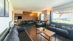 Un salon moderne avec un mur en pierre, des canapés en cuir, une table basse en bois et une grande fenêtre donnant sur la campagne.