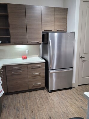 Kitchen features a stainless steel refrigerator, wooden cabinetry, and a white countertop.
