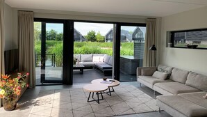 A modern living room with a sofa, a round coffee table, and a view of a garden and buildings through large glass doors.