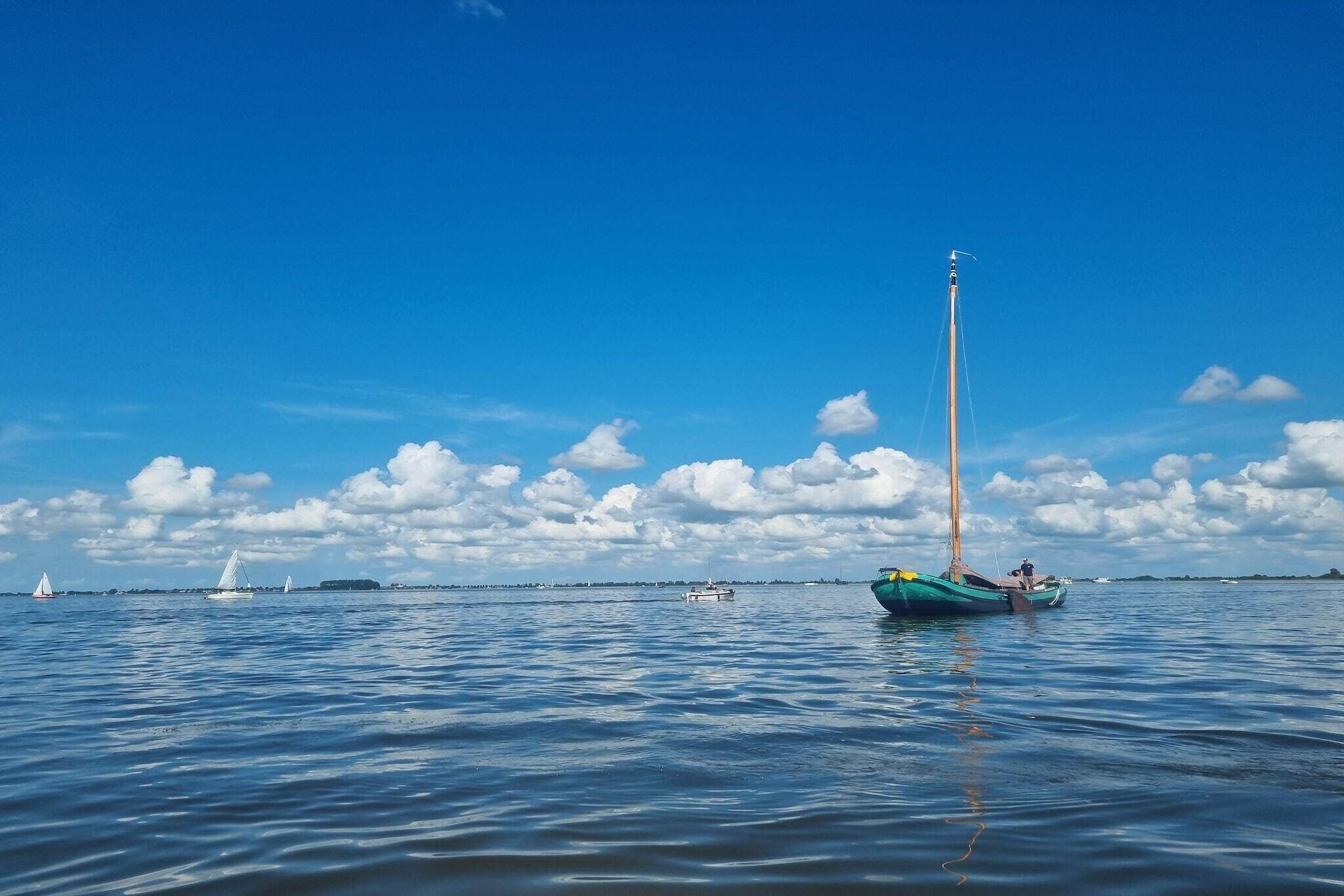 Mar tranquila con veleros, cielo despejado y tierra a lo lejos.