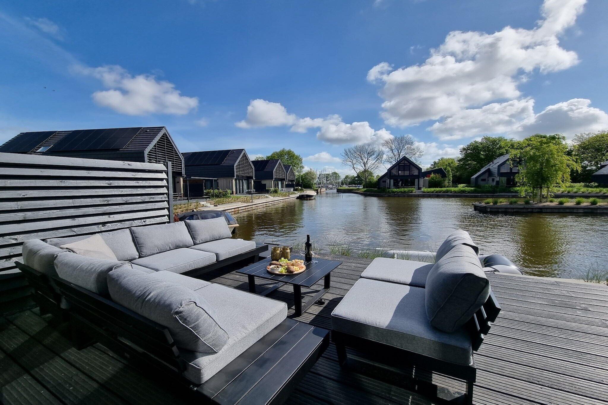 Eine Uferterrasse mit einer Couch, einem Tisch mit Speisen und Blick auf Häuser gegenüber dem Wasser.