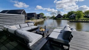 En terrasse ved floden med en sofa, et bord med mad og udsigt til huse over vandet.