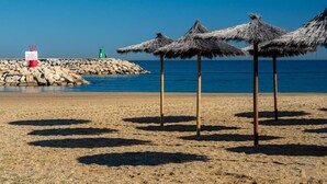 A beach with thatched umbrellas, a rocky breakwater, and a lifeguard tower.