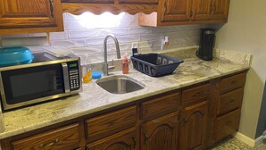 Una cocina con armarios de madera, un lavamanos de acero inoxidable, un microondas y una cafetera.