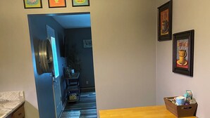 Una cocina con una mesa de madera, un taburete, baldosas de suelo estampadas y cuadros en la pared.