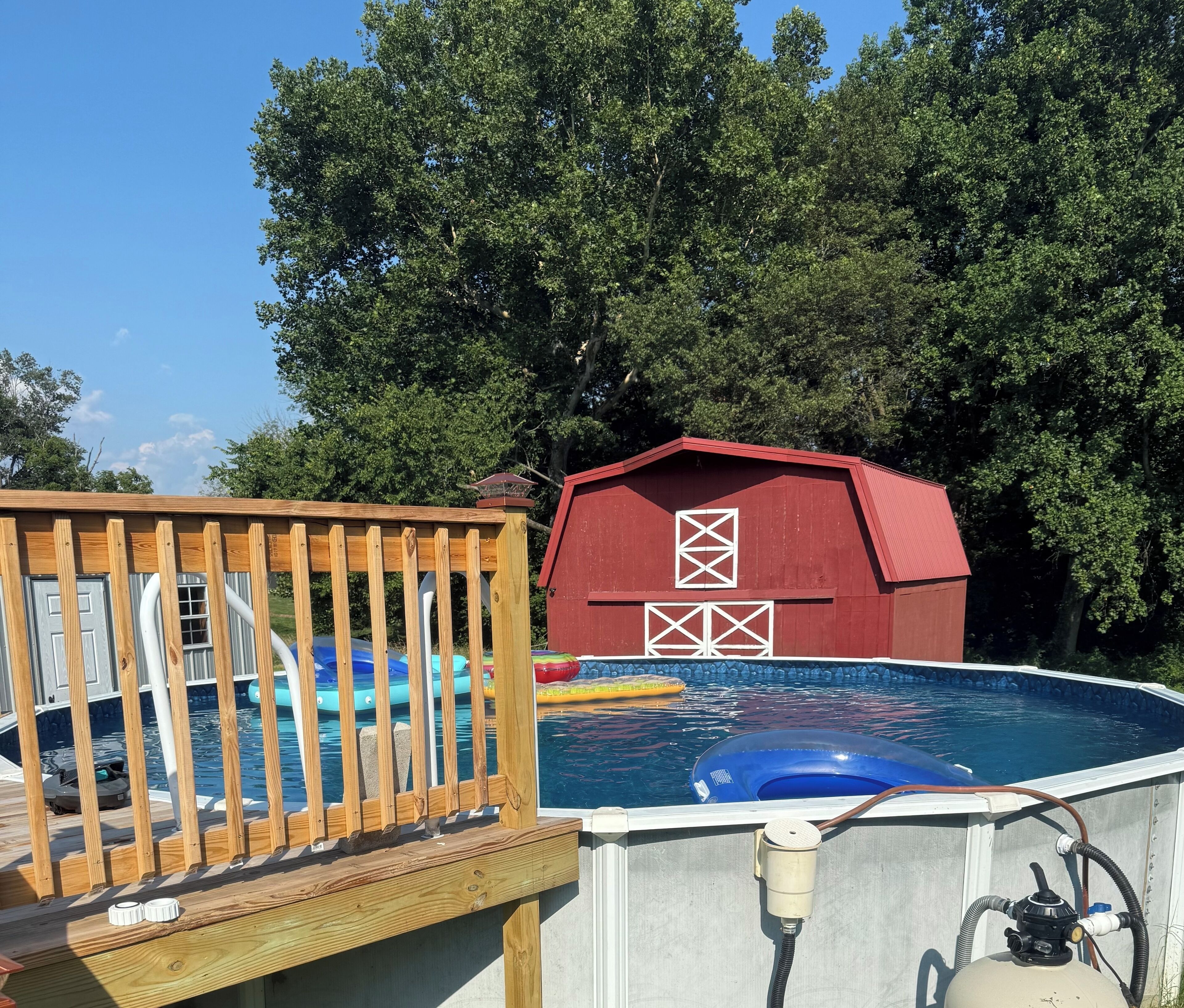Piscina externa com deck de madeira e um celeiro vermelho ao fundo.