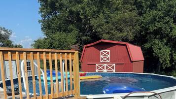 Piscina externa com deck de madeira e um celeiro vermelho ao fundo.