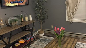 Una sala de estar con televisor, mesa de centro de madera, planta en maceta y un jarrón de tulipanes.