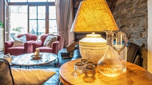 Un salón acogedor con un ventanal grande, un sofá rojo, una mesita de centro y objetos decorativos como una lámpara, una jarra y pequeños jarrones.