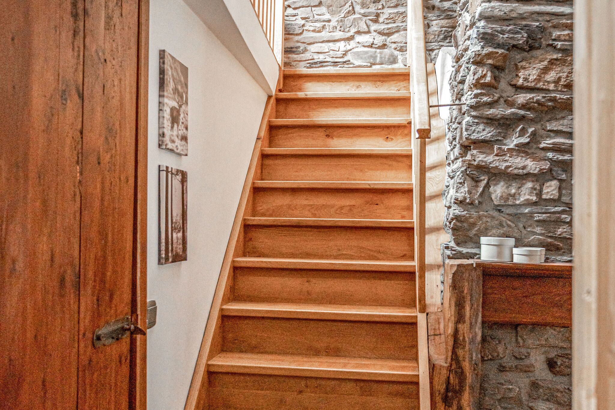 A wooden staircase with a stone wall on one side.