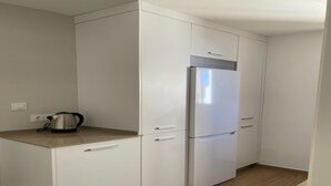 Cocina compacta con muebles blancos, un refrigerador de acero inoxidable y una tetera sobre la encimera.
