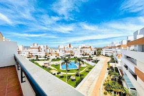 A residential complex with multiple apartment buildings, a central courtyard with a swimming pool, and a clear blue sky.