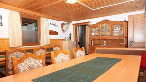 Uma sala de jantar com uma mesa de madeira comprida, cadeiras e um armário com portas de vidro.