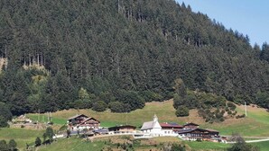 Uma pousada de montanha com vários edifícios, uma igreja e um cenário de floresta.