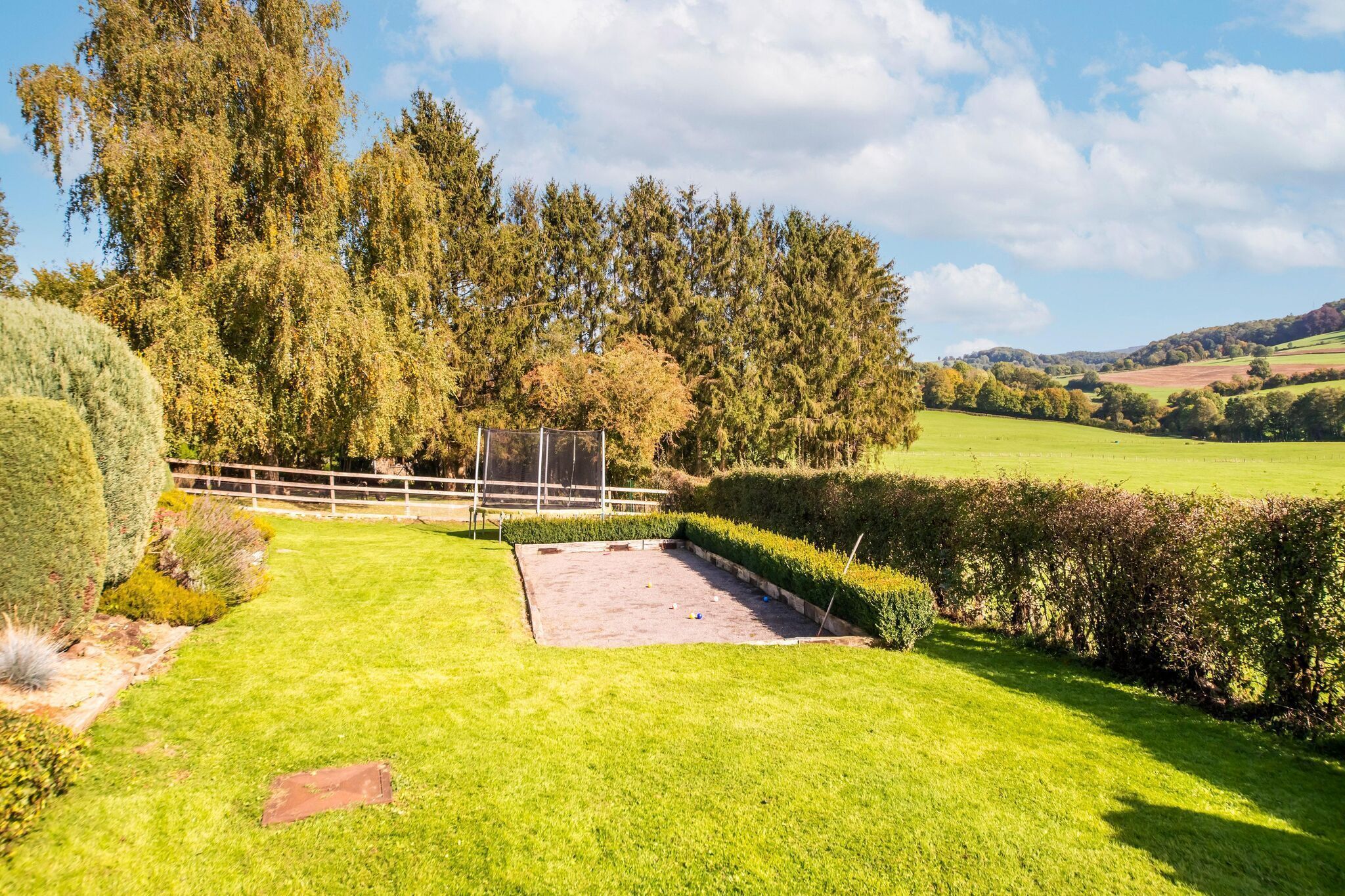 A well-maintained garden with a lawn, a fenced area, and a variety of trees and shrubs.