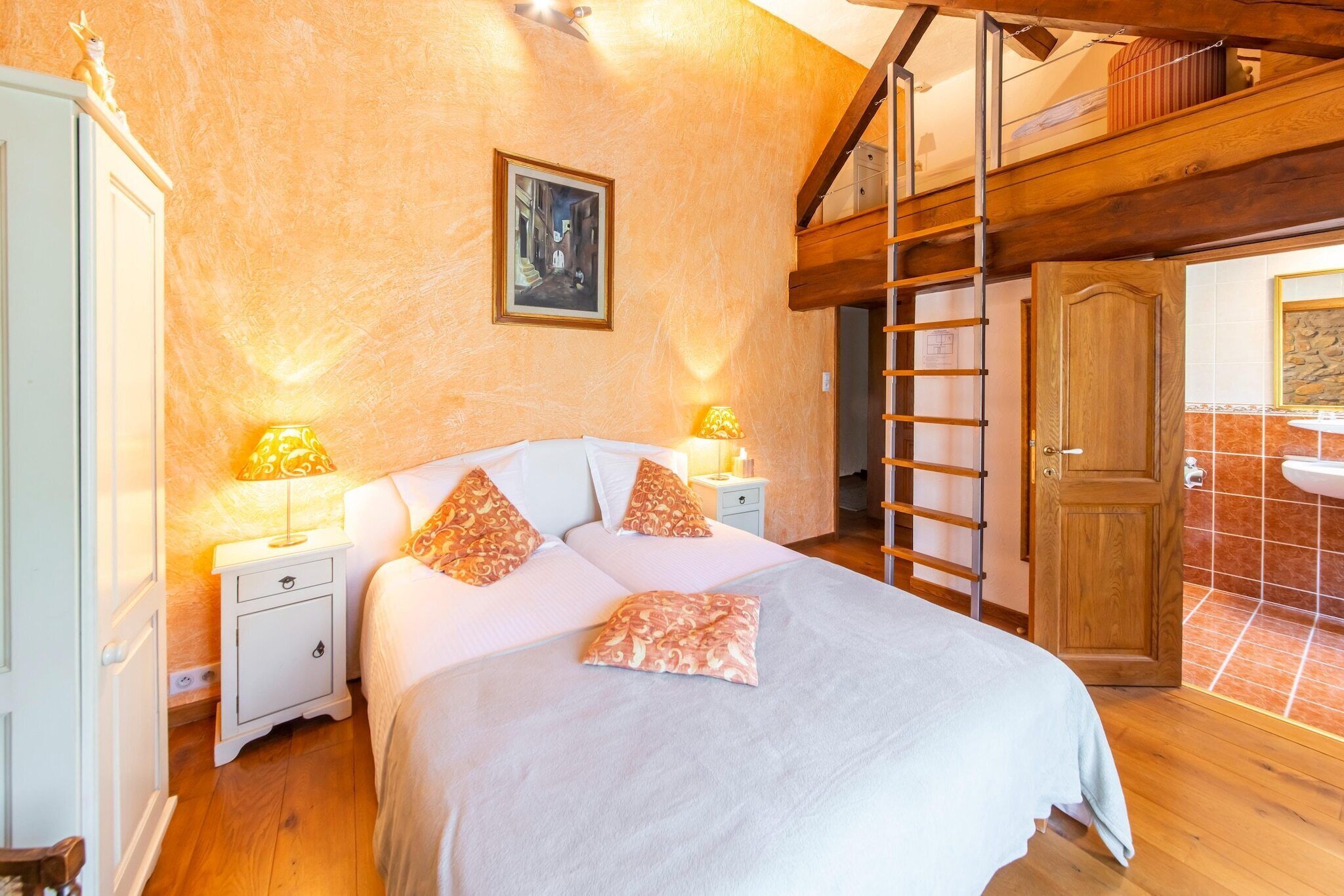 A bedroom with a bed, nightstands, a painting, a wooden ladder, and a bathroom with a sink and tiled walls.