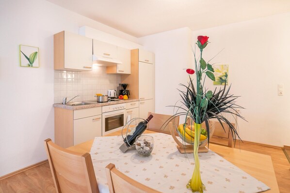 A modern kitchen with white cabinets, a dining table with a vase of flowers, and a coffee machine. - Apartment in Neustift near Ski Lift (Neustift im Stubaital)