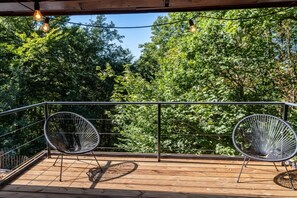 A wooden deck with two wireframe chairs and a heart-shaped shadow on the floor. - Chalet in the woods with Nordic bath (Manhay)