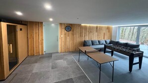A modern living room with a foosball table, a sofa, and a dartboard. - Chalet in the woods with Nordic bath (Manhay)