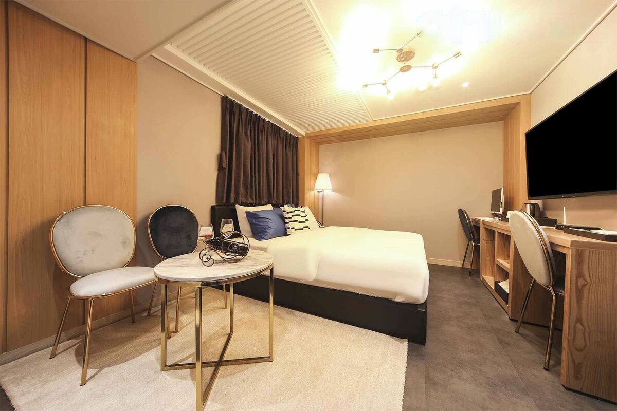 Habitación de hotel con cama, escritorio con ordenador, silla y una pequeña mesa redonda con lámpara.
