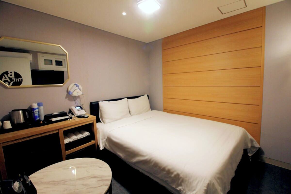 Una habitación de hotel con cama, escritorio con teléfono, espejo y estante con artículos de aseo.