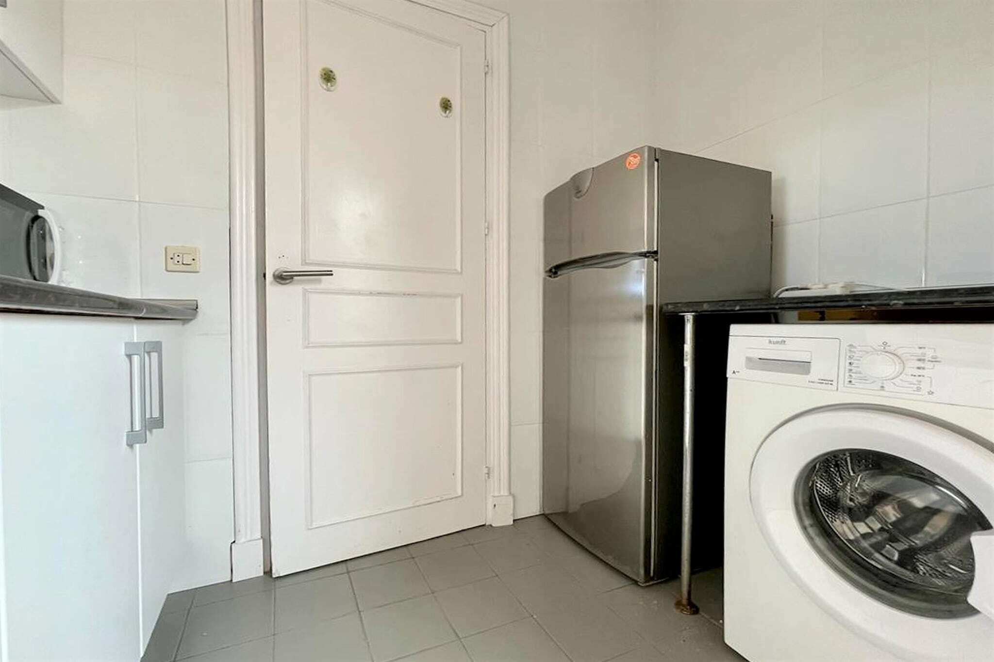 Cocina compacta con refrigerador, lavadora y una puerta con picaporte.