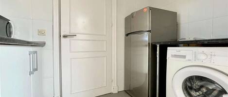 Cocina compacta con refrigerador, lavadora y una puerta con picaporte.