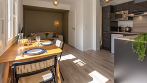 Una cocina moderna con armarios oscuros, microondas y cafetera. Hay una zona de comedor con una mesa y sillas de madera, y un sofá al fondo.