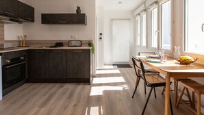 Una cocina moderna con armarios oscuros, horno empotrado y comedor con mesa y sillas de madera.