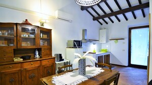 A dining area with a wooden table, chairs, and a vase. There is a kitchen area with cabinets, a microwave, and a window. - Charming Family Retreat in Umbria (Mantignana)