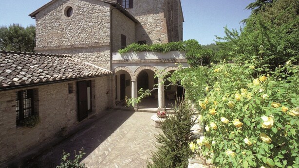 A stone building with a courtyard, arched entrance, and a rose bush. - Charming Family Retreat in Umbria (Mantignana)
