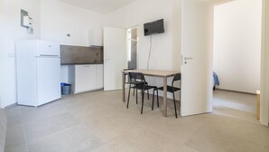 Une cuisine compacte équipée d’un réfrigérateur, d’une cuisinière et d’un four à micro-ondes. Un coin repas avec une table et des chaises est également disponible. Un téléviseur est fixé au mur.