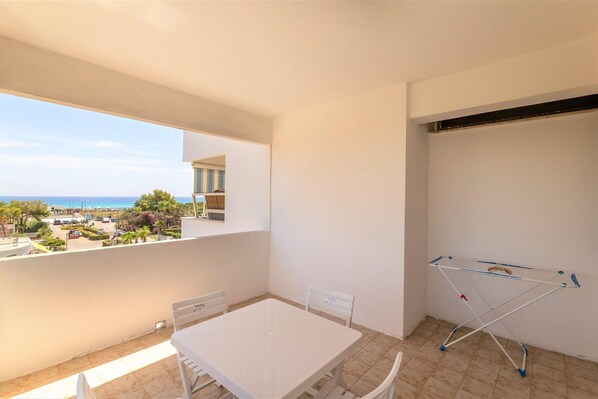 Un balcón con mesa y sillas, un tendedero y vistas al mar y edificios.