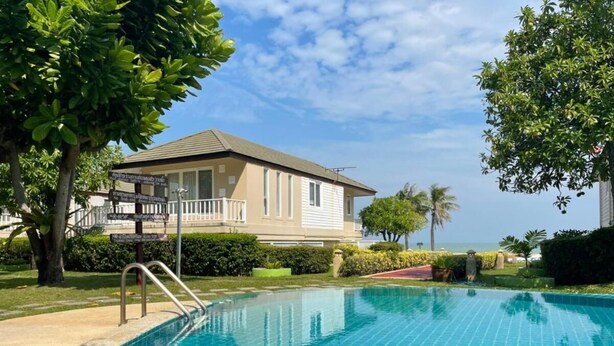 A swimming pool with a clear blue water surface, surrounded by a well-maintained lawn and a building with a balcony. - RIM Chaam By RoomQuest (Cha-am)