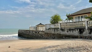 A beach with a concrete wall, a small building, and a fence overlooking the ocean. - RIM Chaam By RoomQuest (Cha-am)