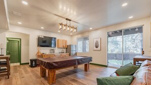 Un vaste salon comprenant une table de billard, un canapé en cuir et une grande porte-fenêtre coulissante donnant sur un balcon.