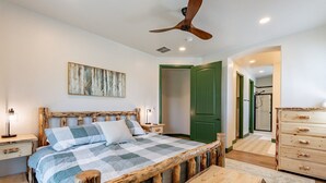 Une chambre à coucher avec un lit en bois, un ventilateur de plafond, une porte verte et une commode en bois.
