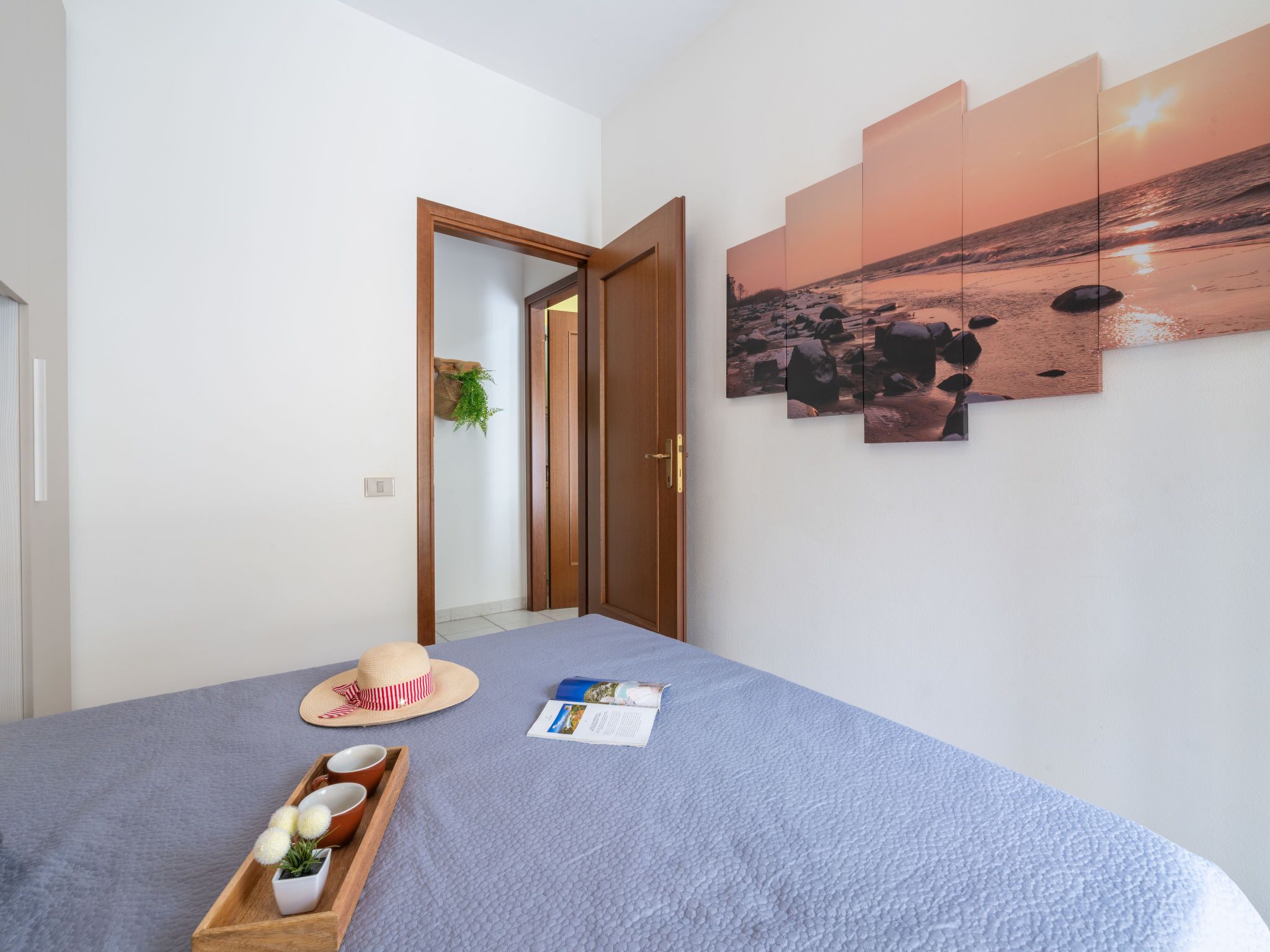 Ein Schlafzimmer mit einem Bett, einer Holztür, einem an der Wand befestigten Regal mit einer Pflanze, einem Hut und einem Tablett mit Tassen und einer Pflanze.