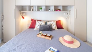 A neatly arranged bedroom with a bed, bedside lamps, a tray with items, and a hat on the bed. - Apartment Iris by Interhome (Villasimius)