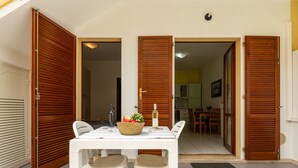 A dining area with a table, two chairs, a fruit bowl, and a bottle of wine. - Apartment Iris by Interhome (Villasimius)